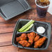 A black Dart foam container with three compartments holding fried chicken legs and celery sticks.