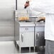 A chef in a white coat uses a Cooking Performance Group countertop fryer to cook food.