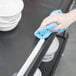 A person cleaning a black utility cart with a blue towel.