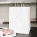 A white Duro paper shopping bag with cupcakes inside.