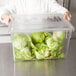 A chef holding a Rubbermaid clear polycarbonate food storage box lid filled with lettuce.