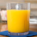 A Cambro clear plastic tumbler filled with orange juice on a table.
