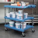 A blue Metro utility cart with three shelves holding white containers of food.