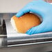 A person in blue gloves using an APW Wyott vertical conveyor bun grill toaster to toast a bun.