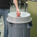 A person using a Rubbermaid funnel top to throw a can into a trash can.