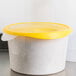 A white Rubbermaid polyethylene food storage container with a yellow lid on a counter.
