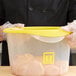 A person in gloves holding a Rubbermaid yellow plastic food storage container with chicken inside.