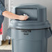 A man putting a white cloth in a grey Rubbermaid dome top for a 55 gallon trash can.