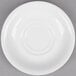 A close-up of a 5 1/2" bright white porcelain saucer on a gray surface.