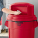 A person putting a bag into a red Rubbermaid dome top for a 55 gallon trash can.