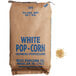 A brown bag of Reist white large butterfly popcorn kernels next to a pile of white popcorn.