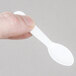 A hand holding a Solo white plastic taster spoon.