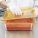 A person in gloves using a Rubbermaid amber high heat food pan lid to hold a container of food.