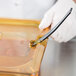 A person in white gloves using a tool to cut food in a Rubbermaid plastic food pan with a notched amber lid.