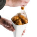 A hand placing fried chicken into an American Metalcraft cardboard fry cone.