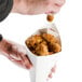 A person holding a square cardboard fry cone filled with fried chicken.