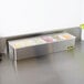 A San Jamar stainless steel condiment bar on a counter filled with trays of fruit and vegetables.
