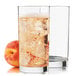 A Libbey Lexington cooler glass of liquid with ice next to a glass of ice and a peach.