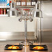 A Hanson Heat Lamps freestanding heat lamp with dual bulbs over plates of food on a countertop.