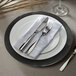 A black glass charger plate with silverware and a napkin on it.