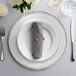 A Charge It by Jay gold beaded glass charger plate with a white napkin and silverware on a table.