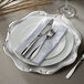A Charge It by Jay silver plastic charger plate with silverware on a white napkin.