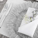A Charge It by Jay silver glass charger plate with a white napkin and flowers on it.