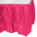 A Creative Converting hot magenta pink plastic table skirt with a pleated edge on a table.