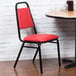 A red Lancaster Table & Seating banquet chair with black legs sits next to a table.