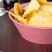 A raspberry polyethylene round basket filled with potato chips on a table.