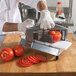 A person using a Nemco Easy Tomato Slicer to slice tomatoes on a cutting board.