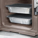 A close-up of a Cambro Granite Sand food pan carrier with food trays inside.