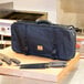 A black Mercer Culinary knife bag with straps on a cutting board with knives.