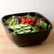 A salad in a black Sabert catering bowl with cucumbers, tomatoes, and lettuce.