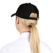A woman with a ponytail wearing a black Chef Revival baseball cap with a white logo.