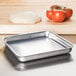 An American Metalcraft square aluminum pizza pan with dough and tomatoes on it.