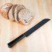 A Fineline black plastic bread knife next to a sliced loaf of bread on a table.