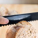 A hand using a Fineline black plastic bread knife to cut a loaf of bread.