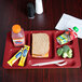 A red Cambro 6 compartment tray with food and drinks including a sandwich, a drink, and a snack.