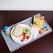 A Cambro slate blue dietary tray on a table with a sandwich, chips, and a drink.