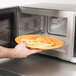 A hand holding a plate of french fries in a Vollrath stainless steel commercial microwave.