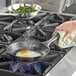 A person cooking two eggs in a Vollrath stainless steel non-stick fry pan on a stove.