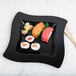 A sushi roll on a Fineline black plastic square plate.