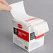 A hand holding a Cambro StoreSafe dissolvable product label roll over a box.