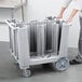 A person pushing a Cambro dish caddy cart with several columns of dishes inside.