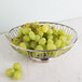 An American Metalcraft stainless steel oval basket filled with green grapes on a marble surface.