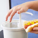 A person's hand using a Cambro clear container to hold a hot dog with mustard.