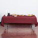A burgundy rectangular plastic table cover on a table with food.