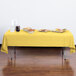 A rectangular yellow Creative Converting plastic table cover on an outdoor table with food.
