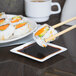 A 3" square white porcelain plate with a sushi roll and chopsticks on it.